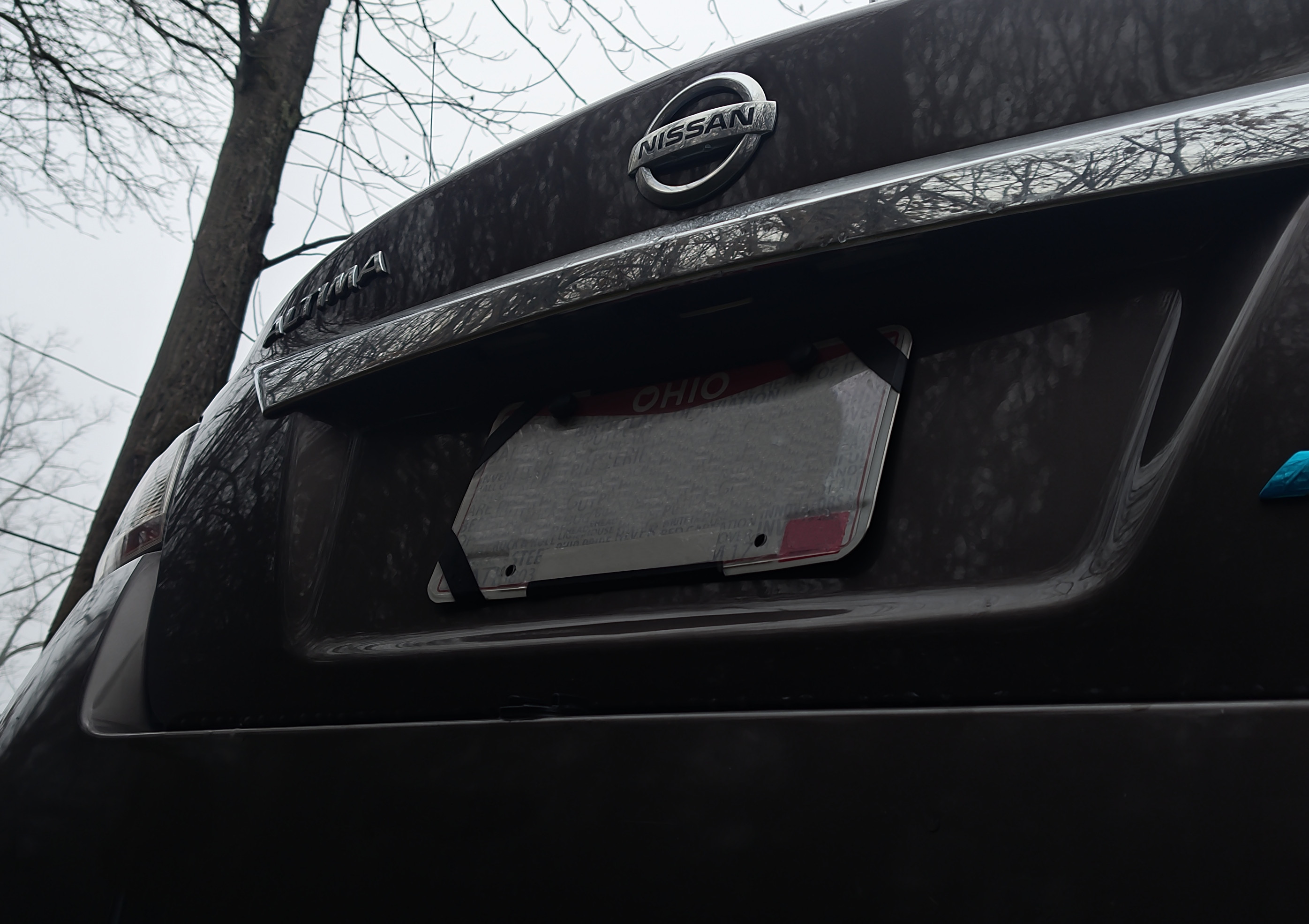 A close-up picture of the back of a brown Nissan sedan, angled up towards the back-up camera above the license plate.