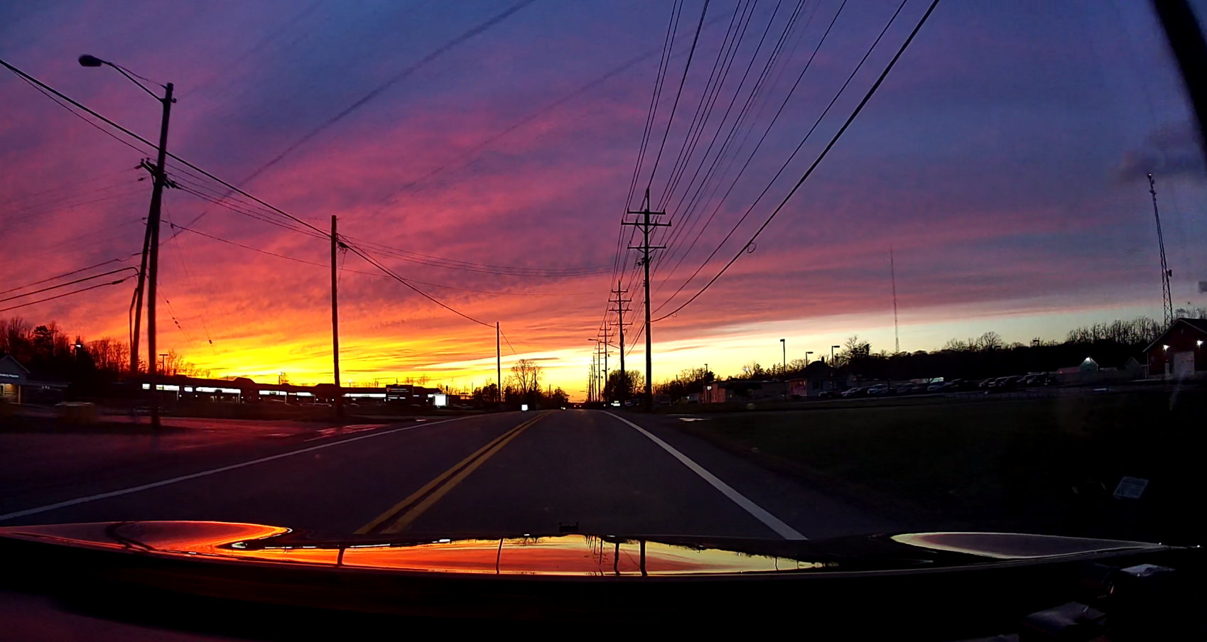 A vibrant orange sunset captured from the perspective of a car driving down the road