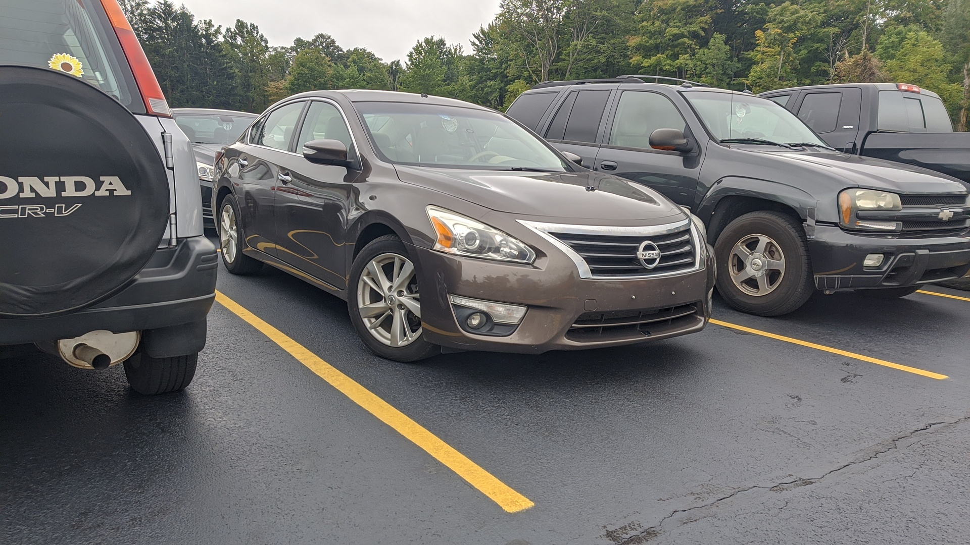 A brown Nissan Altima surrounded by other vehicles in a parking lot
