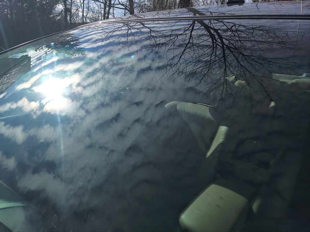 A close up image of a car windshield, with a reflection obscuring a faintly visible dashcam
