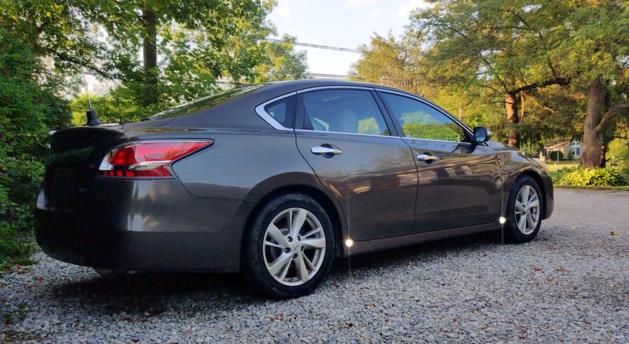 Brown sedan sitting in the shade on a sunny day, with two bright lights on either end of the side fender.