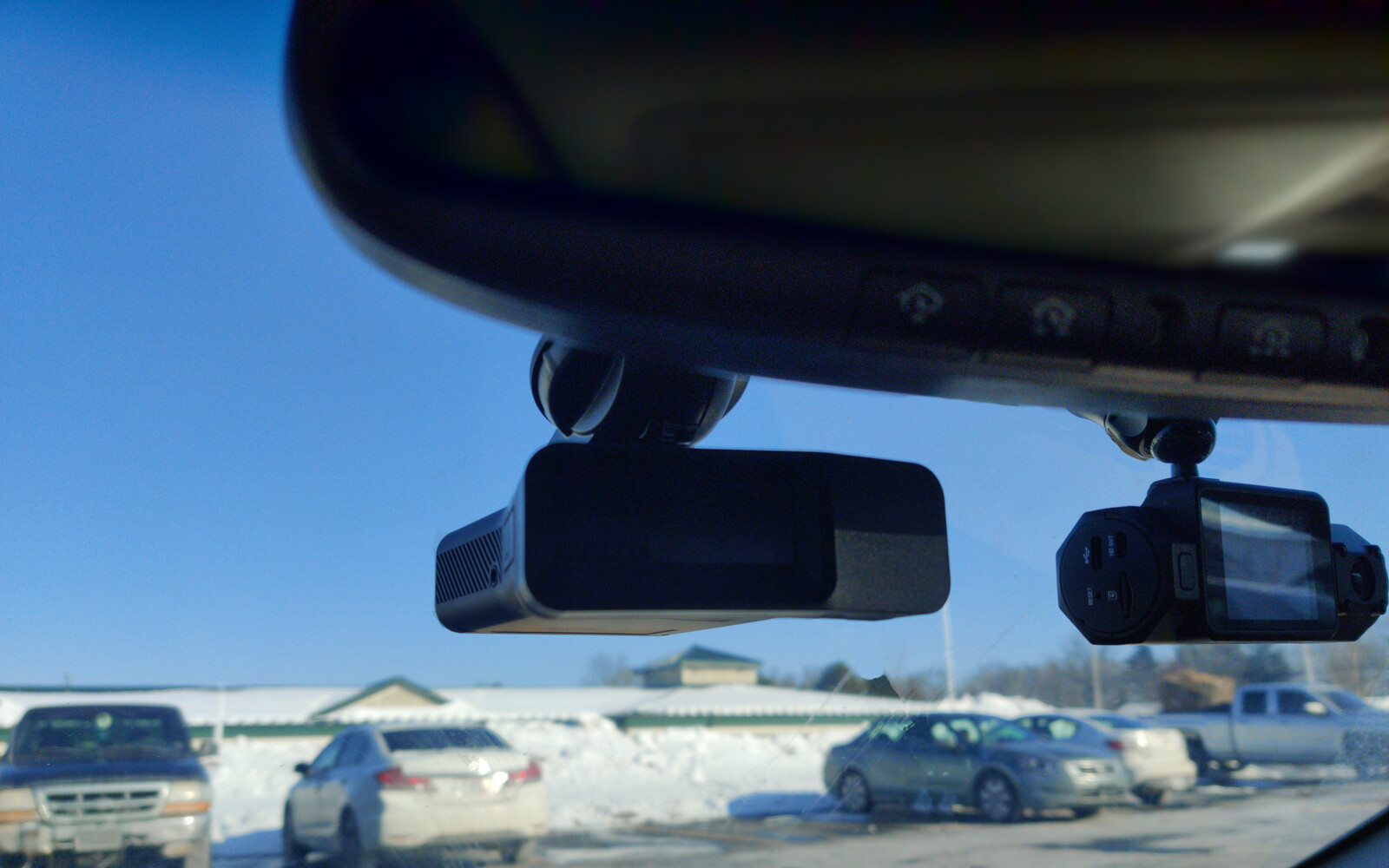 An image of a radar detector and dashcam mounted to the windshield of a car below the rear-view mirror