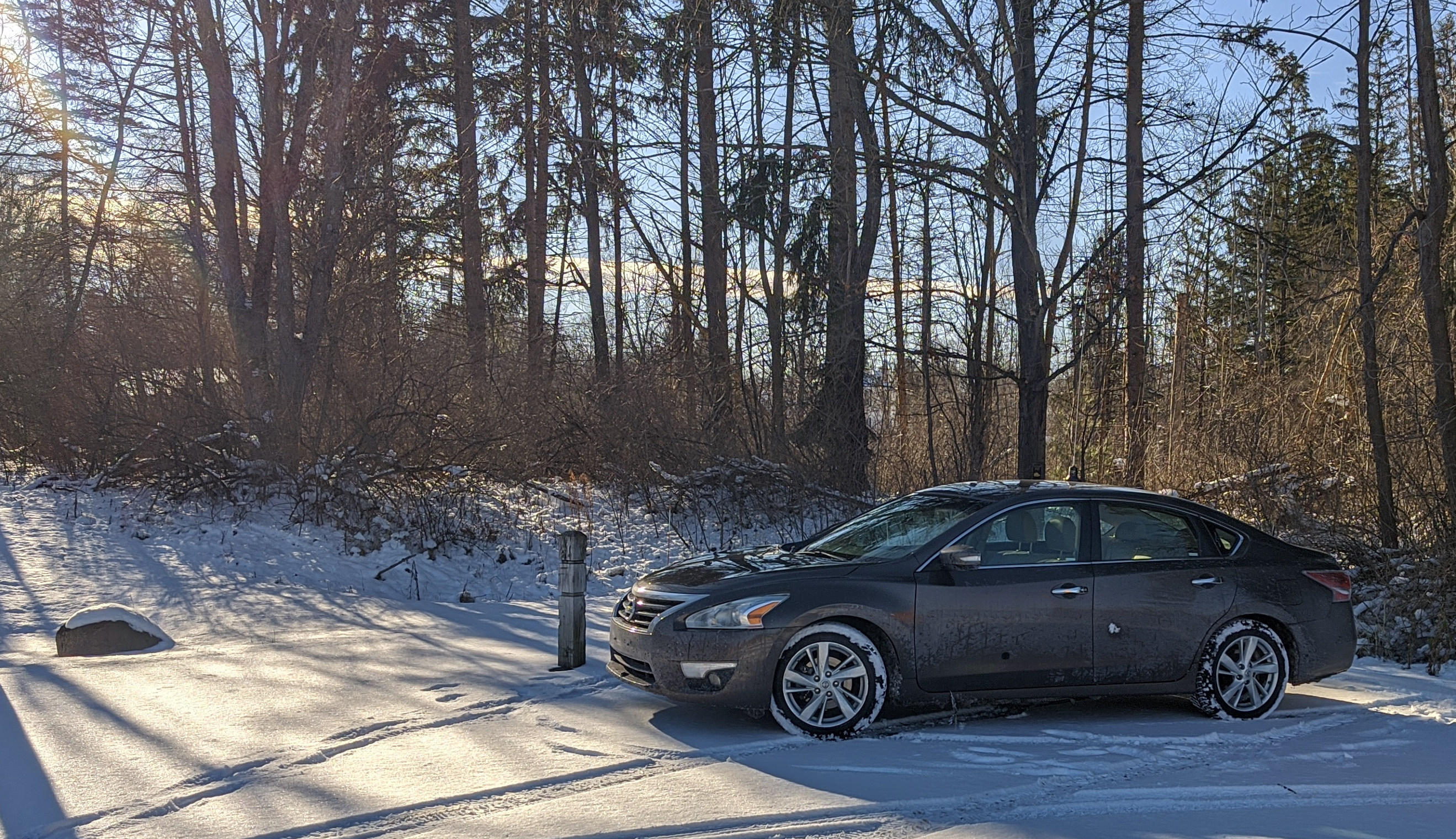 An image of a Nissan Altima with a barely noticable large antenna, parked in a snowy scene with a backdrop of trees